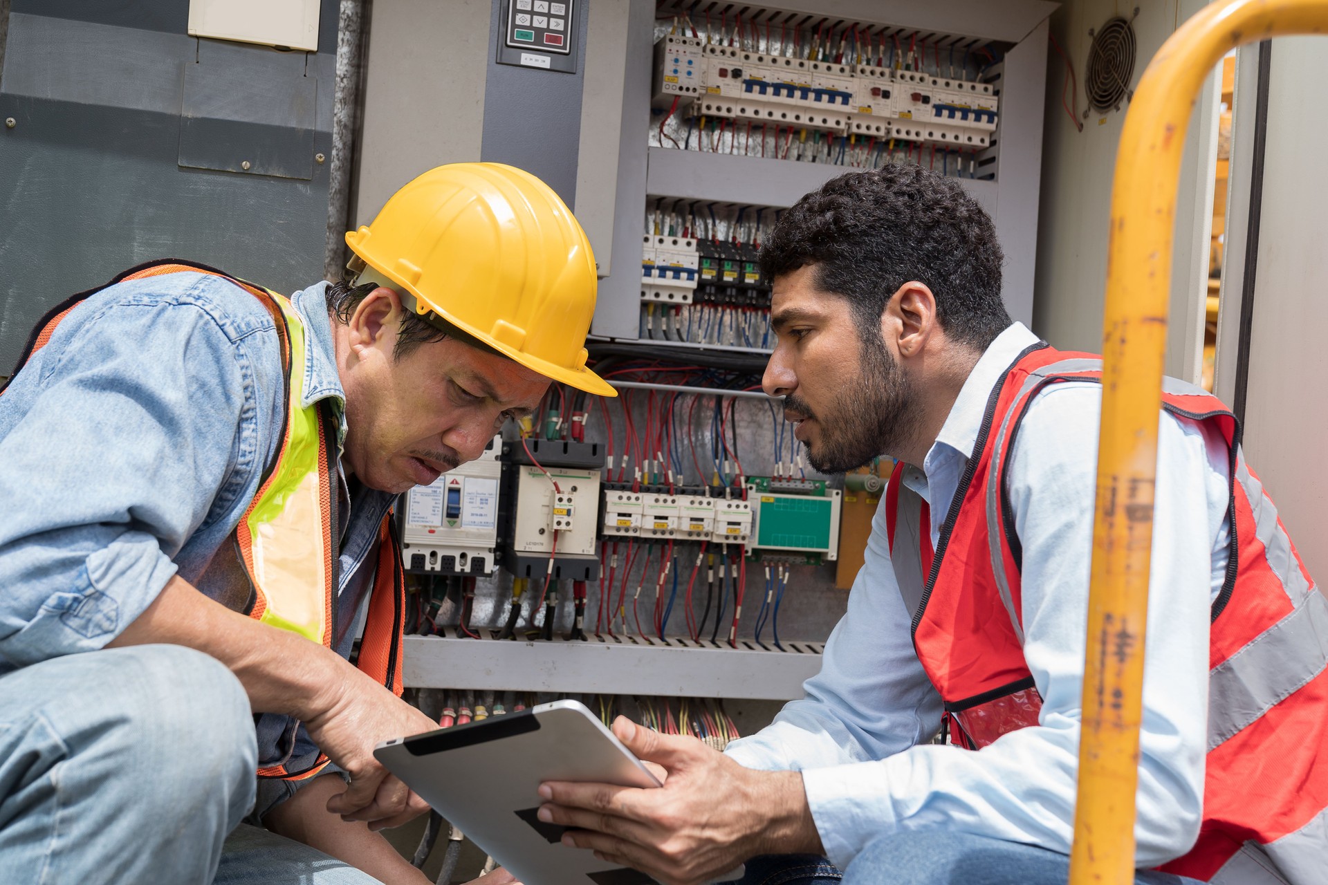 Specialist professional male electrician with digital tablet checking, repair, maintenance operation electric system. Two male electrician using tablet operating electric system in construction site